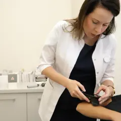 Lekarka w białym fartuchu bada skórę pacjentki na ramieniu za pomocą urządzenia.