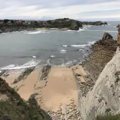 Vista panorámica de la playa San Juan de la Canal, con formaciones rocosas y casas en la costa.