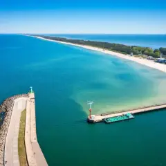 Molo we Władysławowie, z latarnią morską i statkami, wita turystów na piaszczystej plaży.