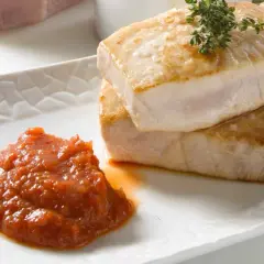 Dos jugosos medallones de atún a la plancha, con sal gruesa y romero, acompañados de una cucharada de salsa de tomate casera.