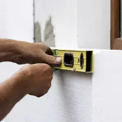 Ręce budowlańca sprawdzają poziomicą, jakie są grubości styropianu przy oknie.