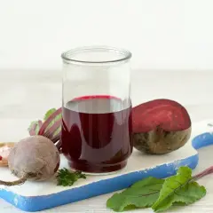Szklanka z sokiem z buraka, obok całe i przekrojone buraki, liście i przyprawy. Pomyśl o zdrowych tabletkach z buraka.