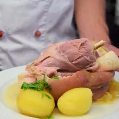 Ein Koch präsentiert ein deftiges Eisbein mit Kartoffeln und Sauerkraut. Die Frage "Eisbein wie lange kochen?" beschäftigt viele Hobbyköche.