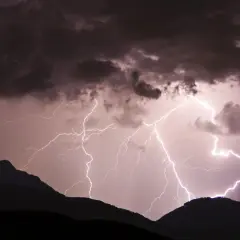 Gewitter in den Bergen: Blitze zucken durch dunkle Wolken über silhouettierten Gipfeln.