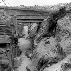 Soldado en posición de combate en las trincheras de la Primera Guerra Mundial. Otros soldados descansan o duermen en el fondo.