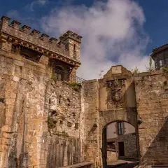 Antigua muralla y arco de entrada en Fuenterrabía, con un escudo nobiliario y un cielo azul con nubes.