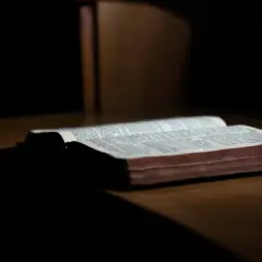 Otwarta Biblia na drewnianym stole, światło pada na strony. Słowa mądrości trwają, dopóki ziemia kręci się.