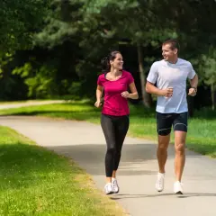 Para biegnie w upale po ścieżce w parku, ciesząc się wspólnym treningiem wśród zieleni.