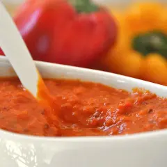 Crema di peperoni bimby in una ciotola bianca, con peperoni rossi e gialli sfocati sullo sfondo.
