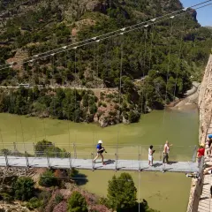 Visitantes caminan por la pasarela del Caminito del Rey, una impresionante ruta del rey entre acantilados y un río verde.