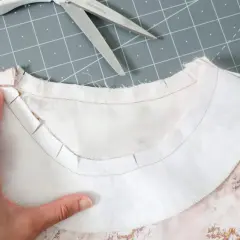 A hand guides the inner facing of a garment, showing the clipped seam allowance for a smooth neckline finish.