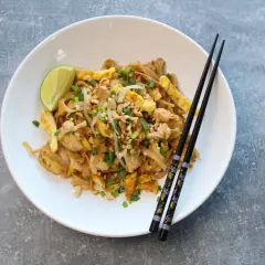 Pad thai z kurczakiem, jajkiem, orzeszkami i limonką na białym talerzu z pałeczkami.