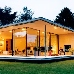 Ein moderner Bungalow mit Glasfronten und einem flachen Dach. Eine Familie entspannt sich auf der Terrasse.