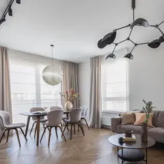 Nowoczesne oświetlenie salonu z jadalnią: designerska lampa nad stołem i reflektory na suficie tworzą przytulną atmosferę.
