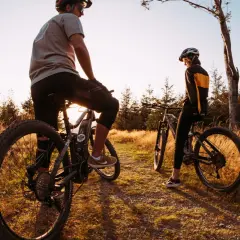 Dwie osoby na rowerach górskich odpoczywają na ścieżce wśród traw. Idealne miejsce na odkrywanie tras rowerowych Śląsk.