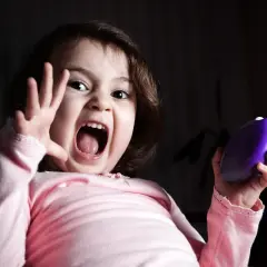 Niña con expresión de miedo, gritando y levantando una mano. Sostiene un objeto morado. Representa el miedo en niños de 6 a 12 años.