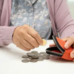 Starsza osoba liczy monety obok portmonetki. Opiekun medyczny zarobki – czy wystarczą na życie?