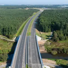 Widok z lotu ptaka na autostradę A1 otoczoną lasem, z mostem nad rzeką.