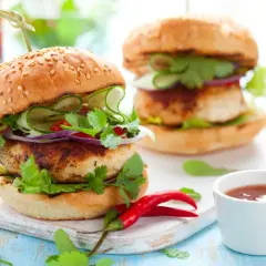 Dos hamburguesas de pollo frescas y jugosas, adornadas con pepino, cebolla morada, cilantro y chile rojo.