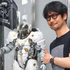 Hideo Kojima z kciukiem w górę obok postaci z gry, z logo Kojima Productions w tle.