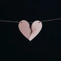 Un cuore di carta rosa, spezzato a metà, pende da un filo. Simbolo di un amore non corrisposto.