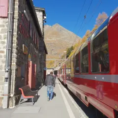 En man går längs en tågstation i bergen, redo för sin tågluffa Europa rutt. En röd tågvagn står parkerad.