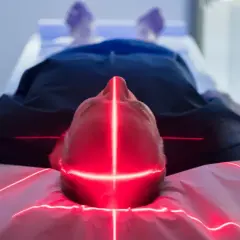 Mann liegt unter roten Laserlinien, die auf seinen Kopf zielen. Dies ist Teil einer neuen Krebstherapie.