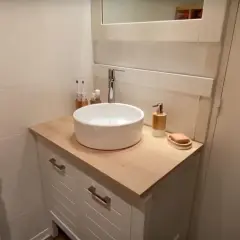 Un meuble de salle de bain relooké avec un plan de travail en bois clair, une vasque blanche et des accessoires modernes.