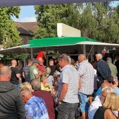 Menschen genießen den feierabendmarkt heute. Viele stehen an einem Imbisswagen, andere sitzen an orangefarbenen Tischen.