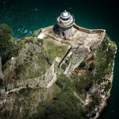 Dos personas caminan por un sendero empinado hacia el faro de caballo, un faro solitario en un acantilado rocoso sobre el mar turquesa.