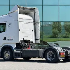 Biała Scania R420 z logo "Erik Hoek Transport" stoi przed nowoczesnym budynkiem z zielonymi oknami.