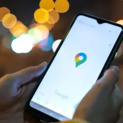 Dłoń trzyma smartfon z otwartą aplikacją Mapy Google. W tle rozmyte światła miasta. Idealne, by sprawdzić, jak znaleźć rozładowany telefon.