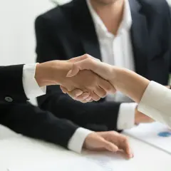 Dwie osoby w garniturach ściskają sobie dłonie, symbolizując udaną współpracę. To właśnie jest trade marketing co to znaczy - budowanie relacji biznesowych.