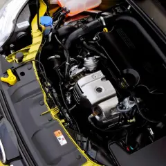 Silnik 1.0 Ecoboost w żółtym Fordzie. Widoczny jest czarny kolektor dolotowy z napisem Ecoboost, elementy metalowe i przewody.
