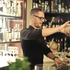 Barman w okularach nalewa drinka. Zastanawiasz się, ile się zarabia jako barman? To zależy od lokalu i doświadczenia.