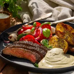 Skivad flankstek med marinad, rostade potatisklyftor, tomatsallad och krämig sås. En perfekt sommarmåltid.