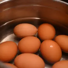 Kilka brązowych jajek w garnku z wodą. Jedno z nich wygląda na zepsute jajko, bo jest lekko pęknięte.