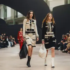 Dwie modelki prezentują kreacje od znanych domów mody na wybiegu. Eleganckie stroje i dodatki przyciągają uwagę widowni.