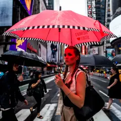 A woman with braided hair holds a bright red umbrella in this 24mm street photography shot. Rain falls on Times Square as people cross the street.