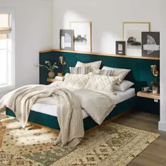 A plush, emerald green headboard with a wooden shelf above offers unique headboard ideas. Artwork and sconces adorn the wall.