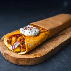 Pyszna shoarma drobiowa z sosem jogurtowym i przyprawami, zawinięta w placek, podana na drewnianej desce.