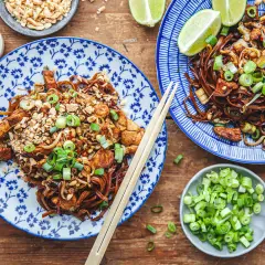 Två tallrikar med läcker pad thai, toppad med jordnötter och salladslök. Ett perfekt pad thai recept för en smakrik måltid.