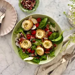 En härlig somrig mat-upplevelse med en fräsch sallad toppad med gratinerad getost på rostat bröd, körsbärstomater, rädisor och nötter.