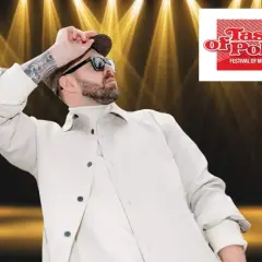Grzegorz Hyży wstaje na scenie Taste of Polonia, w białej kurtce i czapce, w blasku reflektorów.