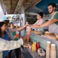 Uśmiechnięci klienci odbierają napoje od barmana w food trucku. Ciekawe, ile zarabia barman za noc przy takiej popularności!