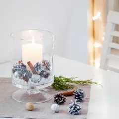 Jak zrobic stroik na stol wigilijny? W szklanym wazonie świeca, szyszki, cynamon i gałązki.