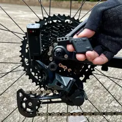 Close-up of a mountain bike's rear derailleur, showing the NX5 electronic shifting system being adjusted by a gloved hand.