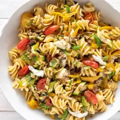 Un piatto invitante di pasta fredda saporita con fusilli, pomodorini, zucchine, peperoni gialli e mozzarella.