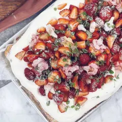 En härlig jordgubbstårta i långpanna, täckt med fluffig grädde och massor av färska jordgubbar, garnerad med blommor och mynta.