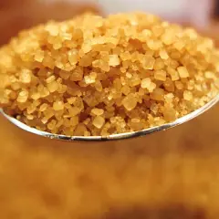 Löffel voller braunem Zucker, der zeigt, wie wird brauner zucker hergestellt: durch Zugabe von Melasse zu weißem Zucker.